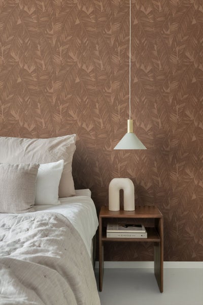 Schlafzimmer mit brauner Vliestapete mit Blattmuster, modernem Nachttisch, Pendelleuchte und Bett mit Textilien in neutralen Tönen.