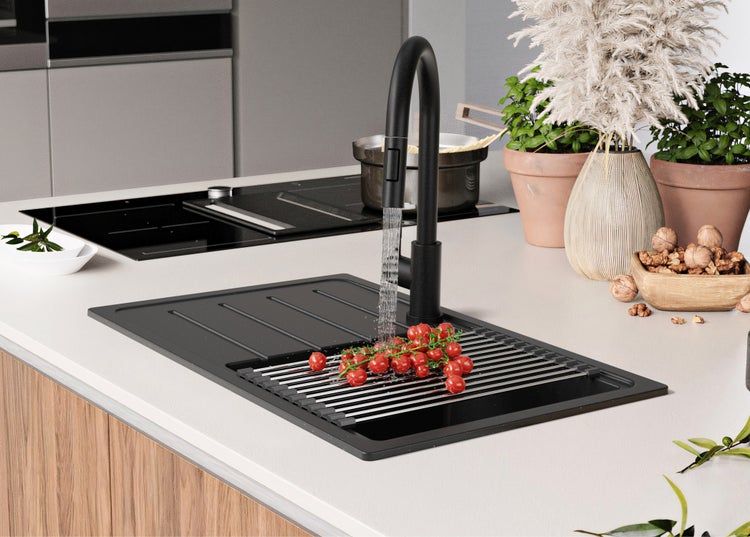 Schwarze Spüle mit Abtropfgestell, Wasserhahn und Tomaten in einer modernen Küche.