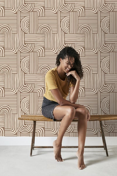 Frau sitzt vor einer Wand mit grafischem Tapetenmuster