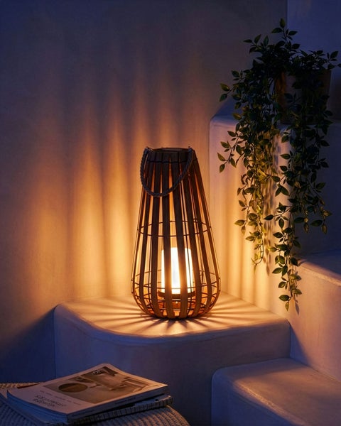 Dekorative Laterne aus Bambusstreben mit Seilgriff, beleuchtet auf einer Stufe neben einer Pflanze stehend.