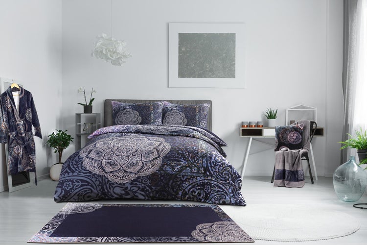 Schlafzimmer mit Bettwäsche im Mandala-Design, passendem Teppich und Bademantel. Hell eingerichteter Raum mit Schreibtisch und Zimmerpflanzen.