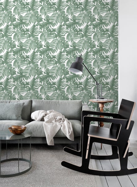 Wohnzimmer mit Sofa, Tisch, Stehlampe, Schaukelstuhl und einer Wand mit Blättertapete.