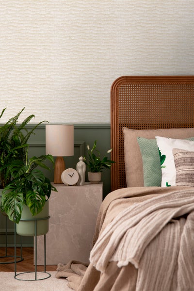 Schlafzimmer mit Rattanbett, Nachttisch, Lampe und Zimmerpflanzen