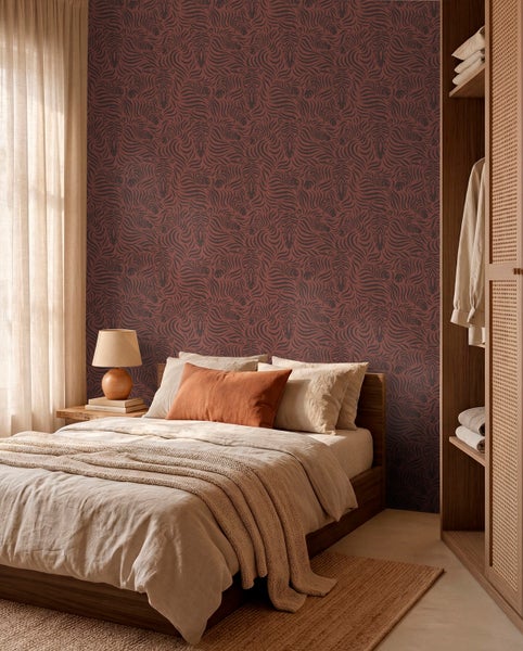 Schlafzimmer mit gemusterter Tapete, Holzbett mit Leinenbettwäsche, Nachttisch mit Lampe und einem Kleiderschrank aus Holz. Warme Atmosphäre.