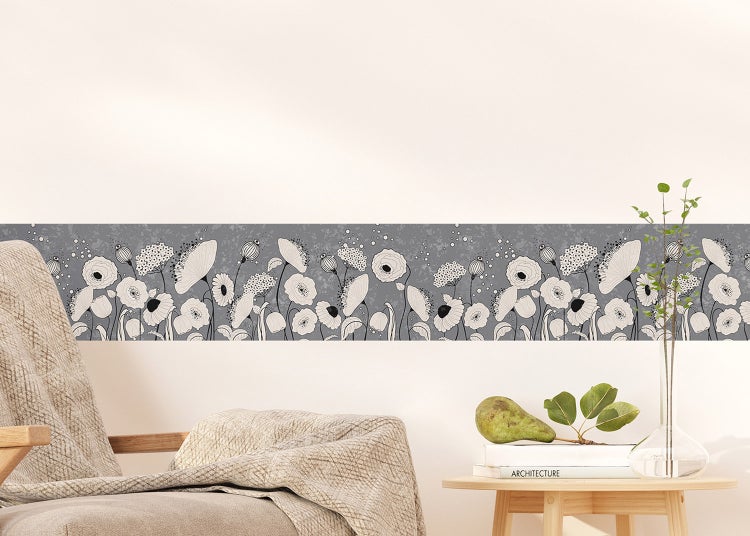 Selbstklebende Tapetenbordüre mit Blumenmuster in einem hellen Wohnzimmer über einem Sessel und einem Beistelltisch.