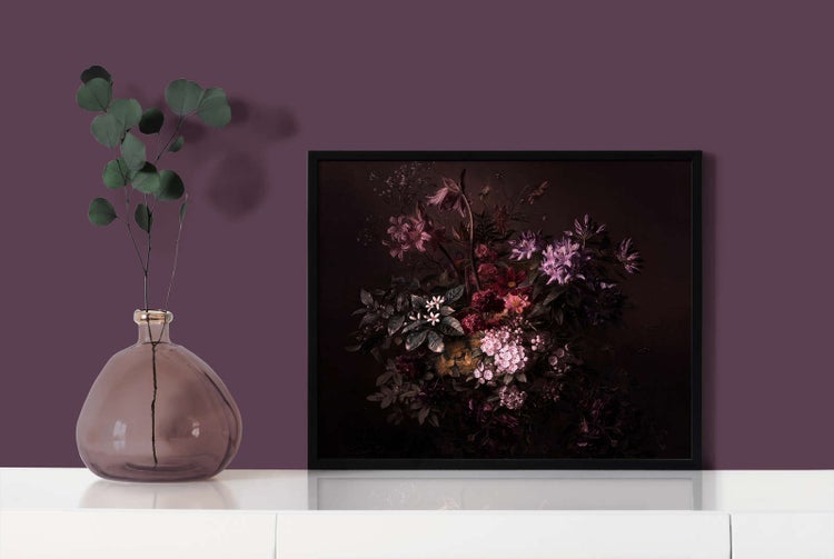 Gerahmtes Wandbild mit dunklem Blumenstillleben in schwarzem Rahmen neben einer Glasvase mit grünem Zweig auf einer weißen Kommode.