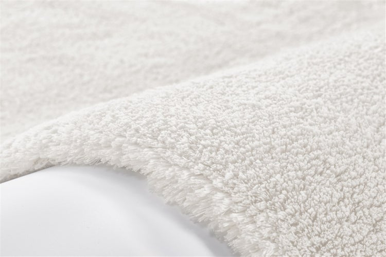 Nahaufnahme eines flauschigen, weißen Hochflor-Badeteppichs aus weichem Material.