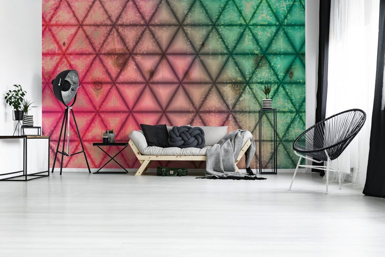 Fototapete mit geometrischem Dreiecksmuster in Holzoptik, Farbverlauf von Rosa zu Grün, modernes Wohnzimmer mit Sofa und Stehleuchte.