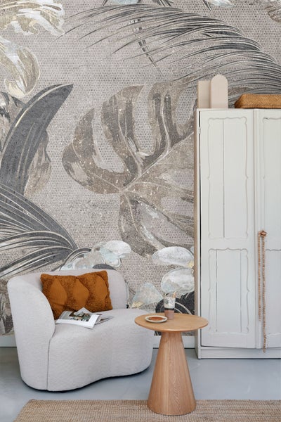 Wohnzimmer mit Sessel, Beistelltisch, Schrank und Fototapete mit Pflanzenmotiven für eine helle und einladende Atmosphäre.