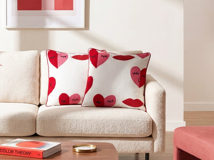 Zwei Dekokissen mit Herz- und Lippenmuster auf einem strukturierten Sofa in einem modernen Wohnzimmer.