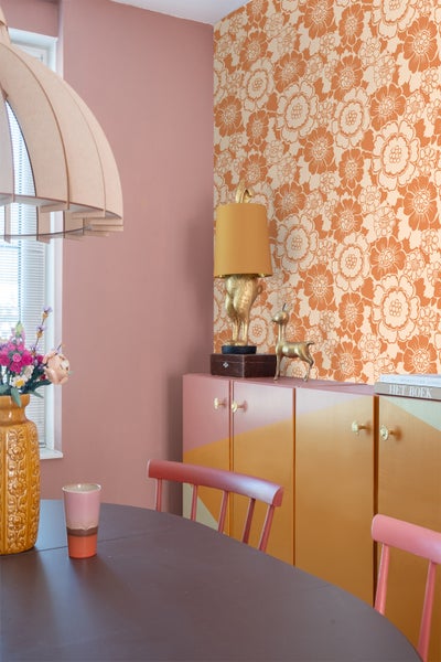 Esszimmer mit Esstisch, Stühlen, Blumenvase, Lampe und Schrank vor einer floralen Tapete