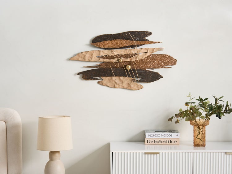 Dekorative Wandkunst aus Metall mit abstraktem Design und goldenen Akzenten über einer weißen Kommode