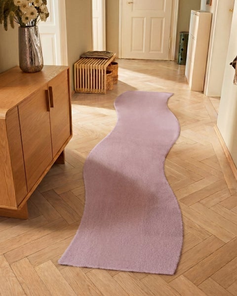 Violetter, wellenförmiger Läufer in einem hellen Flur mit Holzparkett, neben einem Sideboard und einer Sitzbank aus Holz.