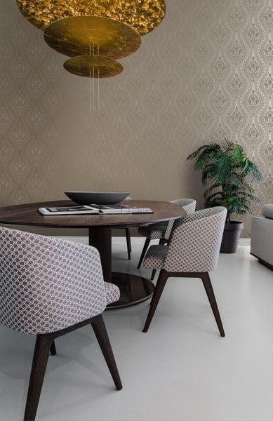 Esszimmer mit rundem Holztisch, Stühlen mit Musterbezug, Zimmerpflanze und gemusterter Tapete