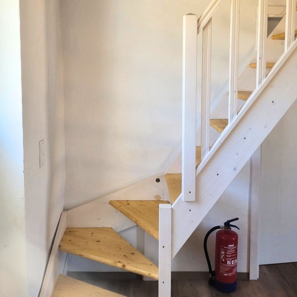 Holztreppe mit weiß gestrichenem Geländer und roter Feuerlöscher