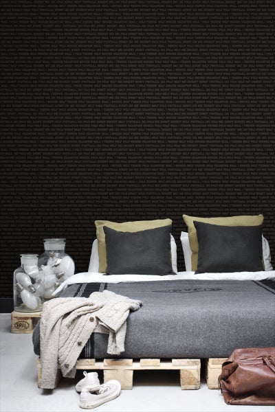 Schlafzimmer mit Bett aus Paletten, Texttapete und dekorativen Gläsern mit Glühbirnen