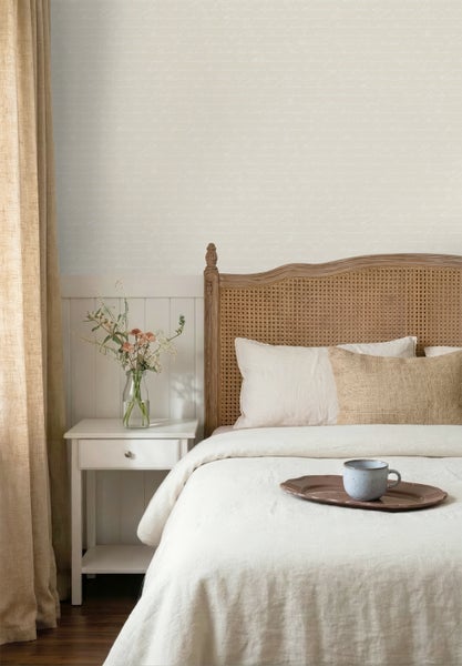 Schlafzimmer mit einer Mustertapete in Schriftoptik, einem Holzbett mit Rattan-Kopfteil und einem Nachttisch.