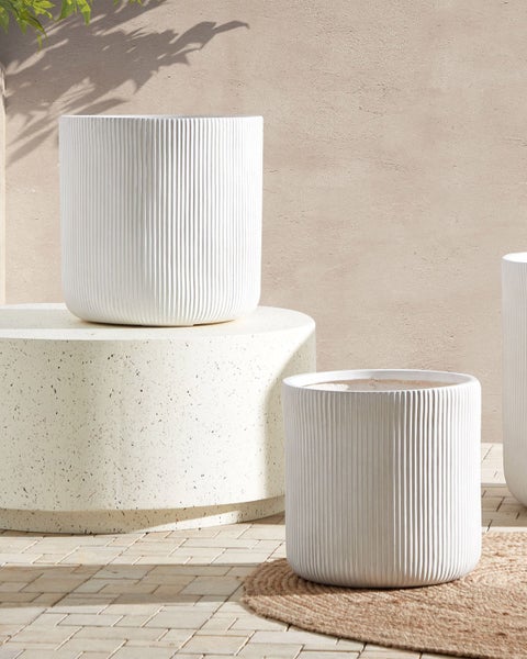 Mehrere weiße Pflanzgefäße mit gerippter Textur in einer Gartenszene.
