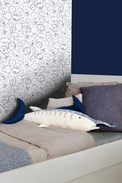 Dekoriertes Bett mit Kissen, Spielzeug und einer Tapete mit Reisepass-Stempel-Motiv