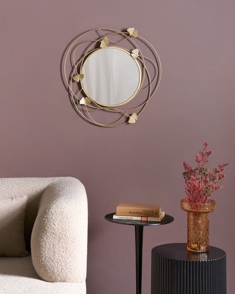 Dekorativer Spiegel mit Metallrahmen in Gold und Blattmotiven über einem Tisch mit Büchern und einer Vase mit getrockneten Blumen.