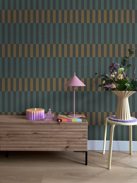 Moderne Raumgestaltung mit geometrischer Tapete in Grün und Gold, einem Sideboard aus Holz und dekorativen Wohnaccessoires.
