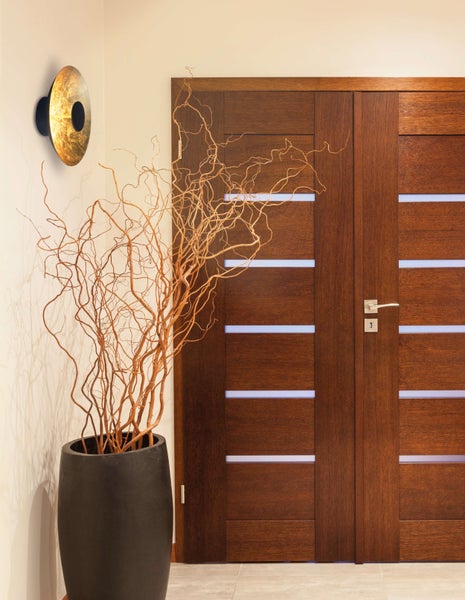 Dekorative Zweige in einer schwarzen Pflanzschale vor einer Holztür und einer runden Wandleuchte