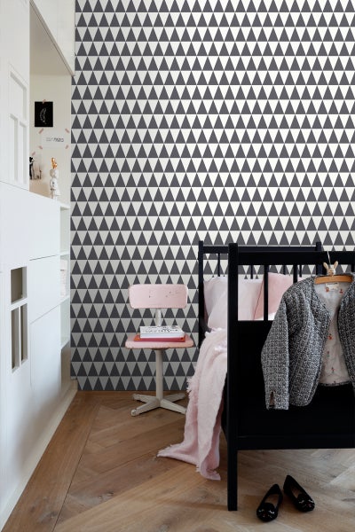 Kinderzimmer mit Tapete mit Dreiecksmuster, Bett, Stuhl und Schrank.