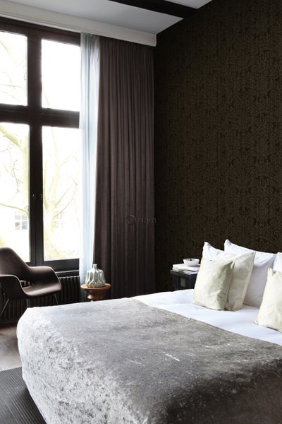 Schlafzimmer mit Bett, Stuhl, Fenster und gemusterter Tapete