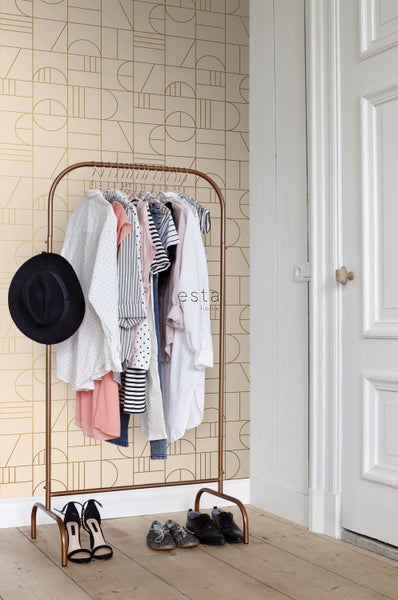 Innenaufnahme mit Kleiderständer, Kleidung und Schuhen vor einer gemusterten Tapete.