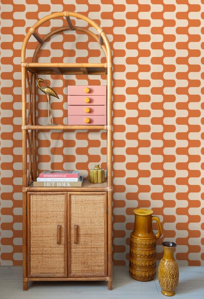 Vliestapete mit orangefarbenem Retro-Wellenmuster hinter einem Bambusregal mit Dekorationsartikeln wie Büchern und Vasen.