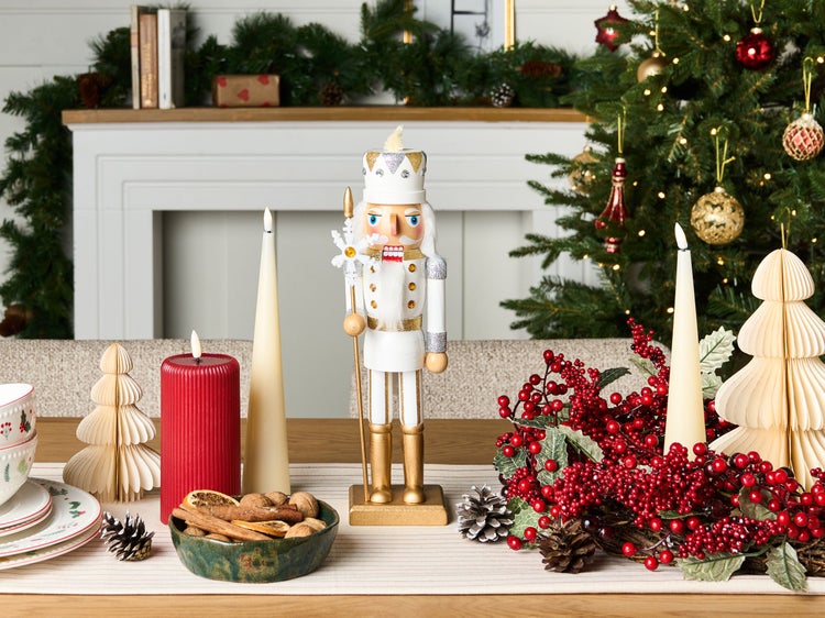 Festliche Dekoration mit Nussknacker, Kerzen und Weihnachtsschmuck auf einem Tisch.