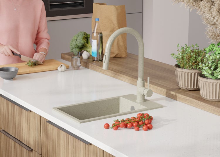 Küchenspüle mit Armatur auf einer Küchentheke, auf der auch Tomaten, Kräuter und andere Lebensmittel liegen.