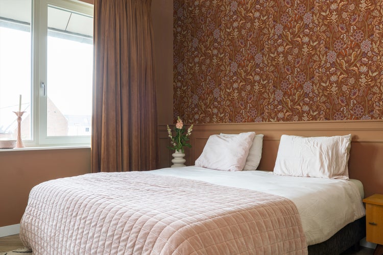 Helles Schlafzimmer mit floraler Tapete, Bett, Kissen und Vorhängen