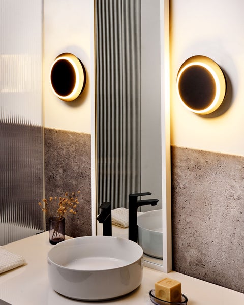 Badezimmer mit rundem Waschbecken, Spiegel und zwei runden Wandleuchten