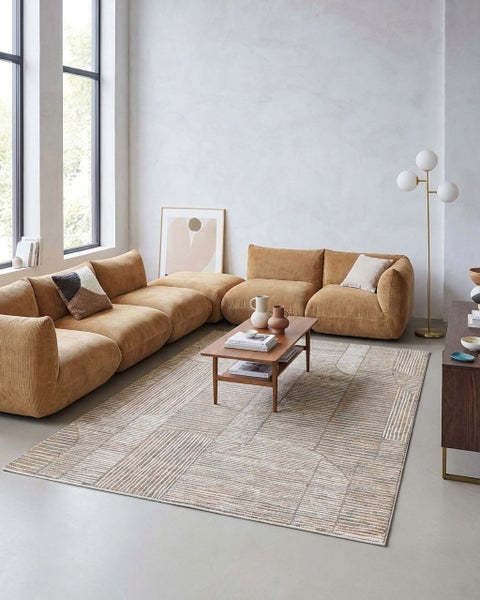 Modernes Wohnzimmer mit einem großen Cordsofa, Holztisch und einem Teppich mit geometrischem Linienmuster in Beige- und Grautönen.