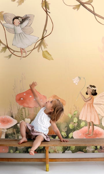Kind sitzt vor einer Tapete mit Märchenmotiven, inklusive Feen und Pilzen.
