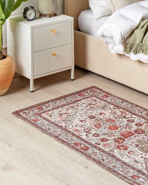 Rechteckiger Teppich mit Vintage-Blumenmuster in einem hellen Schlafzimmer neben weißem Nachttisch und beigem Bett.