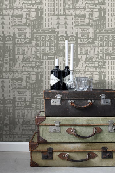 Stapel alter Koffer mit Getränken und Kerzen vor einer Tapete mit Häusermotiven.