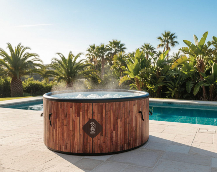 Runder aufblasbarer Whirlpool in Holzoptik mit COCO SPA Logo auf einer sonnigen Terrasse neben einem Swimmingpool und Palmen.