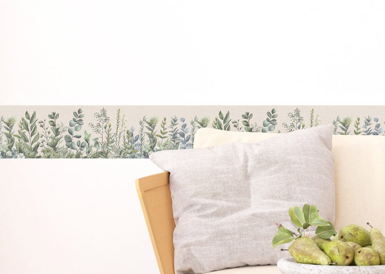 Tapetenbordüre mit botanischem Pflanzenmuster an einer weißen Wand hinter einem Sofa mit Kissen und Birnen.