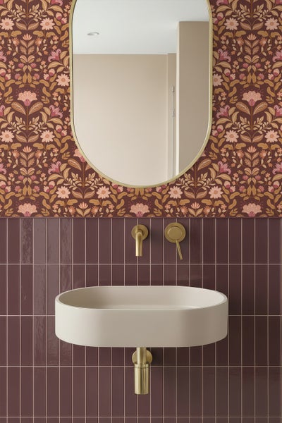 Modernes Badezimmer mit ovalem Spiegel, Blumentapete, dunklen vertikalen Fliesen und hellem Aufsatzwaschbecken mit goldfarbener Wandarmatur.