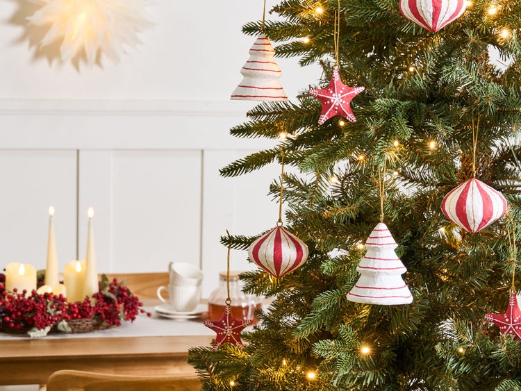 Weihnachtsbaum geschmückt mit rot-weißen Anhängern in Stern-, Baum- und Kugelform, beleuchtet mit warmweißen Lichterketten.