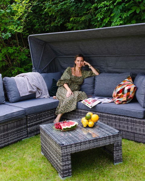 Gartenszene mit Lounge-Set aus Rattan, Tisch und entspannter Frau