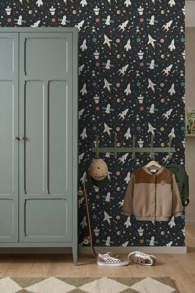 Kindertapete mit Weltraummotiv, Raketen und Planeten auf dunklem Hintergrund im Kinderzimmer neben einem grünen Kleiderschrank.