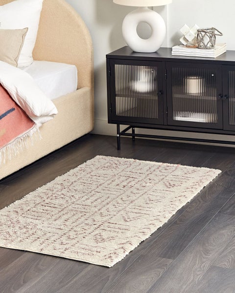 Gemusterter Teppich in Creme und Rosa auf dunklem Boden neben einem gepolsterten Bett und einem schwarzen Metall-Sideboard.