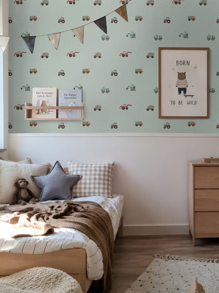 Kinderzimmer mit hellgrüner Tapete mit Baustellenfahrzeug-Motiven, Holzmöbeln und einem Bett mit Zierkissen in einer hellen Atmosphäre.