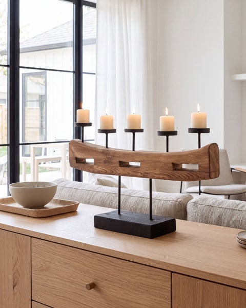 Kerzenständer aus Holz mit fünf brennenden Stumpenkerzen auf einem hölzernen Sideboard in einem modern eingerichteten Wohnzimmer.
