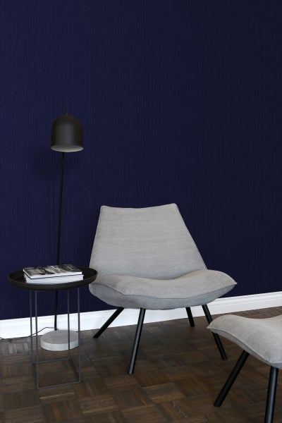 Raumszene mit Sessel, Beistelltisch mit Büchern und Stehlampe vor einer dunklen Wand