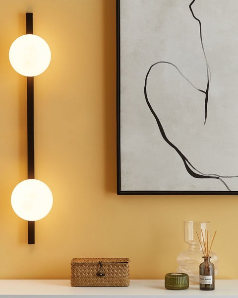 Wandleuchte mit zwei Glaskugeln und ein gerahmtes Bild mit abstrakter Zeichnung auf einer Kommode