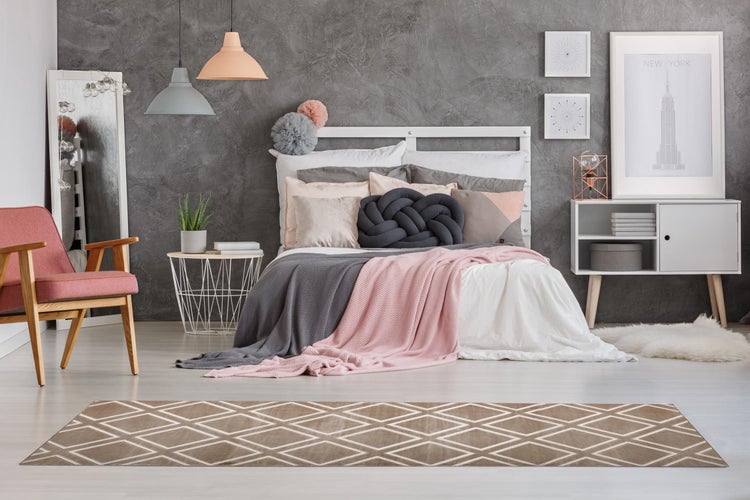 Detailansicht eines beigen Teppichs mit weißem geometrischem Muster und dunkler rutschfester Unterseite mit Noppenstruktur.